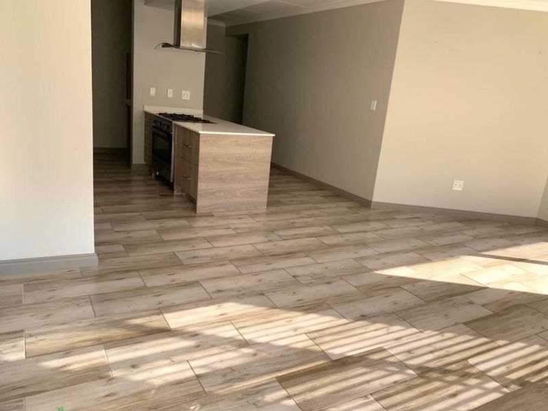 An open-plan living and kitchen area featuring modern wood-look tile flooring, a central kitchen island with a built-in oven, and a stainless steel extractor fan.