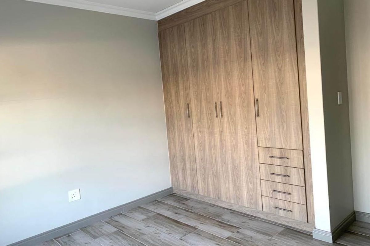A clean, modern bedroom featuring wood-look tile flooring and extensive built-in wooden cabinetry with integrated drawers.