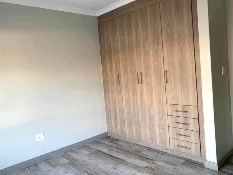 A clean, modern bedroom featuring wood-look tile flooring and extensive built-in wooden cabinetry with integrated drawers.