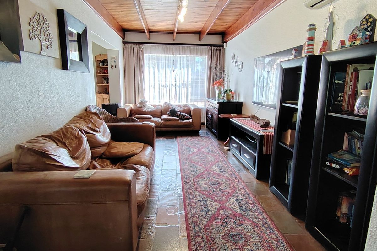 A living room featuring exposed timber beam ceilings, tiled flooring, and an air conditioning unit, providing a cozy and functional living space.