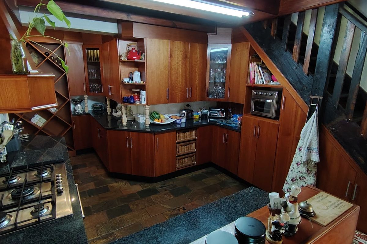 A rustic-style kitchen featuring extensive wooden cabinetry, granite countertops, a gas hob, and integrated oven, positioned beneath a wooden staircase.