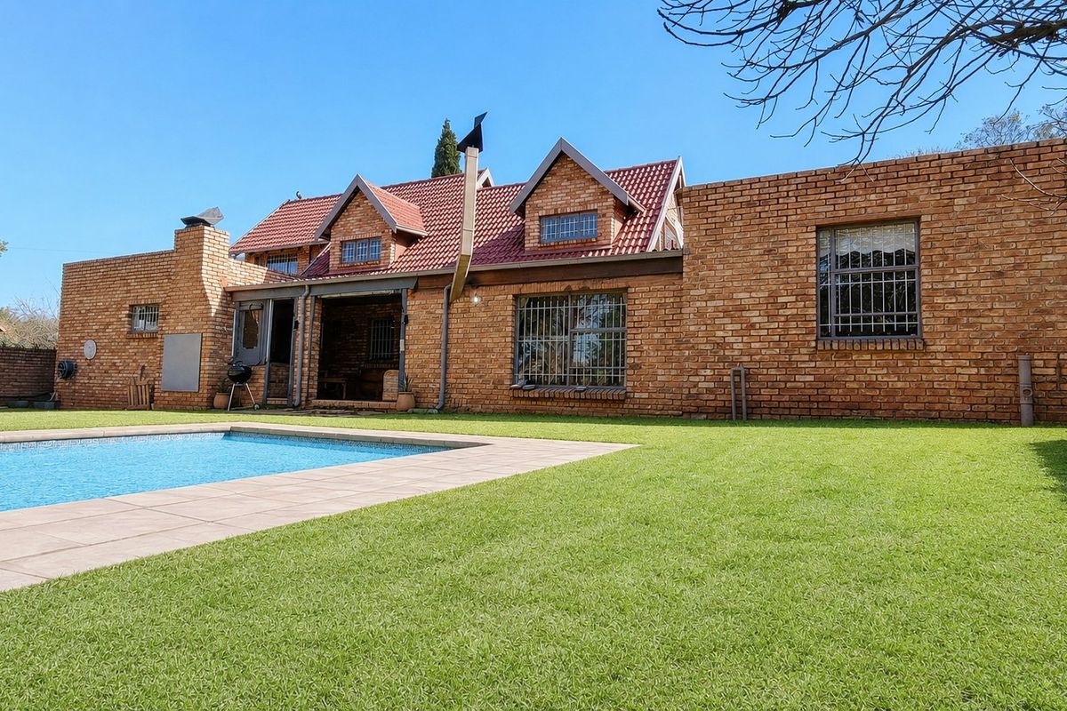 Rear view of a face-brick house featuring a swimming pool, paved surround, and a well-maintained lawn.