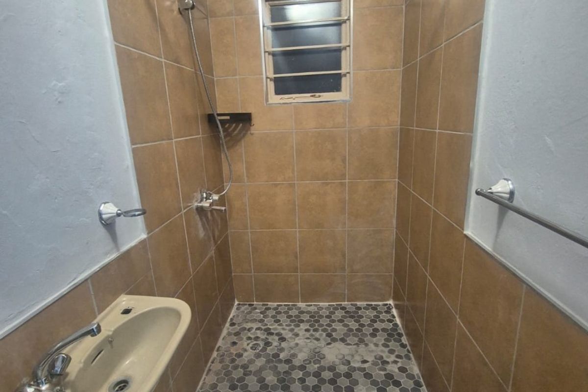A functional bathroom featuring a tiled shower enclosure, basin with mixer tap, and louver window, providing a practical and compact wash area.