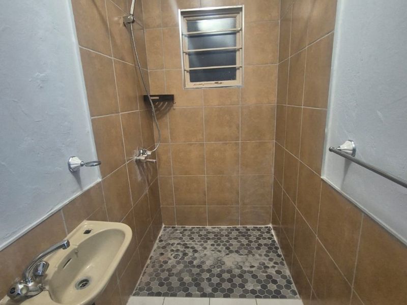 A functional bathroom featuring a tiled shower enclosure, basin with mixer tap, and louver window, providing a practical and compact wash area.