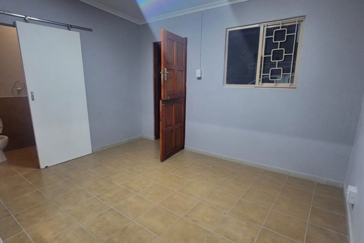 An empty bedroom featuring tiled flooring, a sliding door, and a window with security bars.