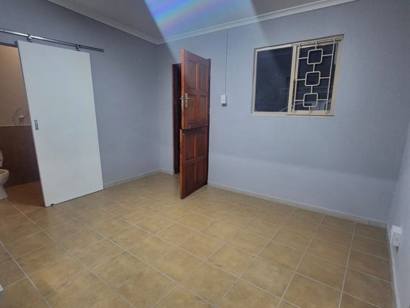 An empty bedroom featuring tiled flooring, a sliding door, and a window with security bars.