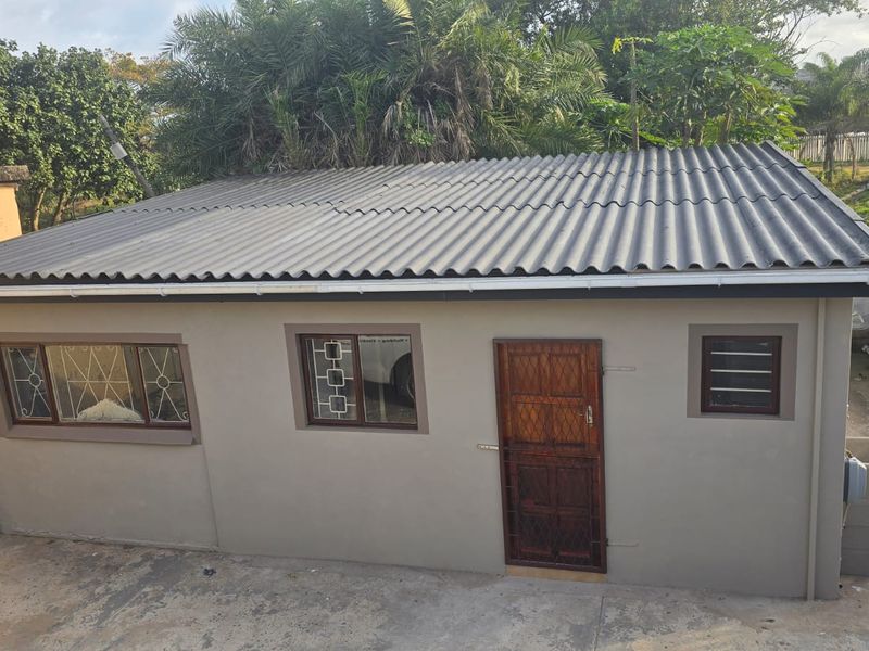 An elevated view of a detached outbuilding featuring a corrugated metal roof, aluminium windows, and an external utility sink area.