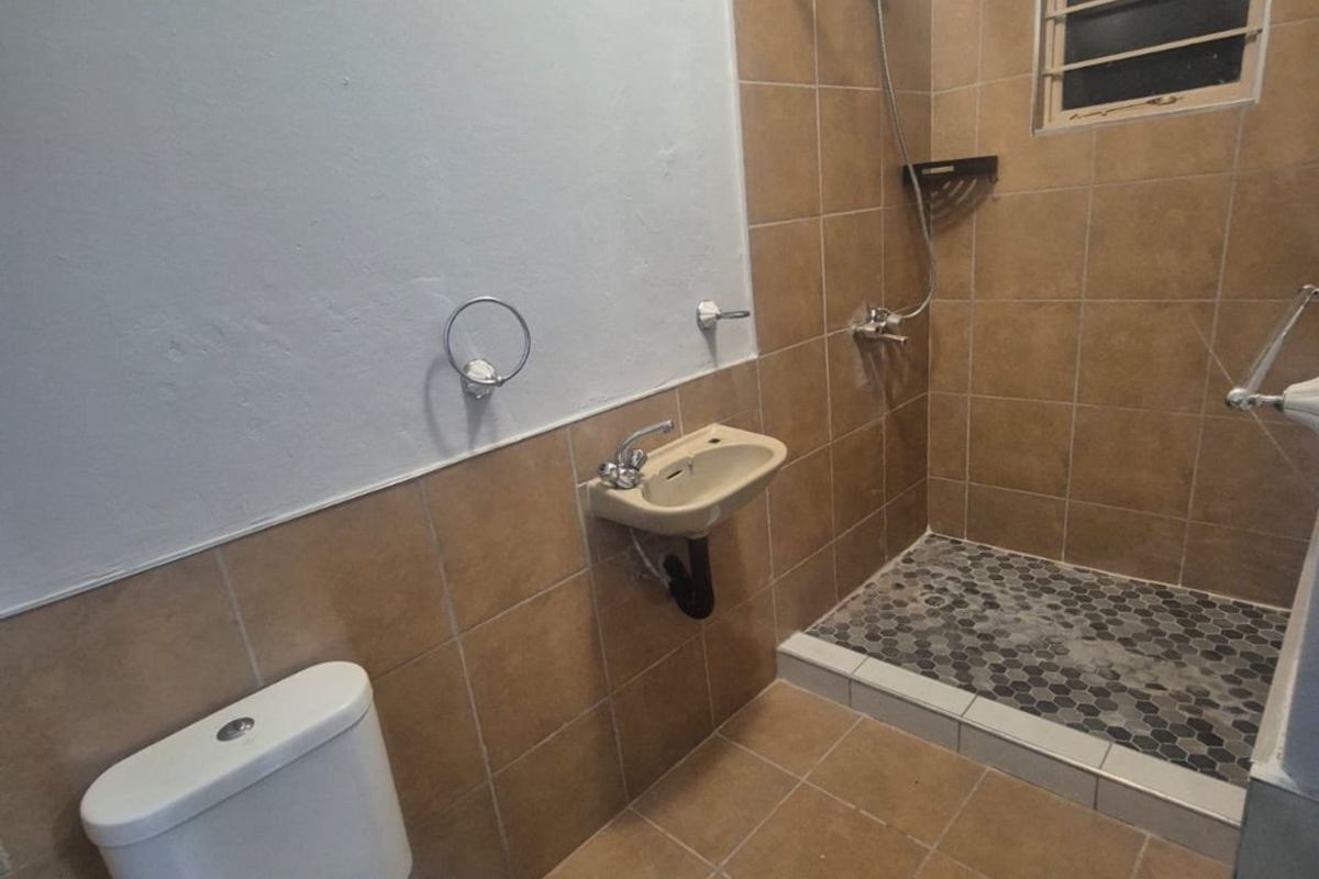A functional bathroom featuring a walk-in shower with tiled flooring, a wall-mounted basin, and a standard toilet, requiring some cosmetic updates.