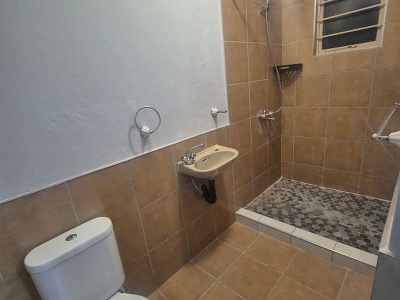 A functional bathroom featuring a walk-in shower with tiled flooring, a wall-mounted basin, and a standard toilet, requiring some cosmetic updates.