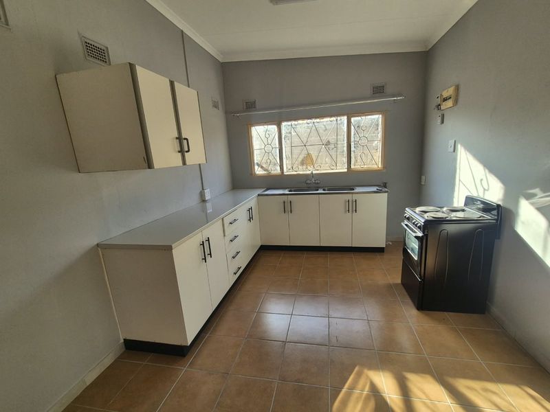 A functional kitchen featuring white built-in cabinetry, a double sink, tiled flooring, and a freestanding stove, offering a clean and practical workspace.