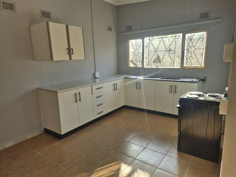 A functional kitchen featuring built-in cabinetry, a double sink, and tiled flooring, offering a clean and practical space ready for updates.