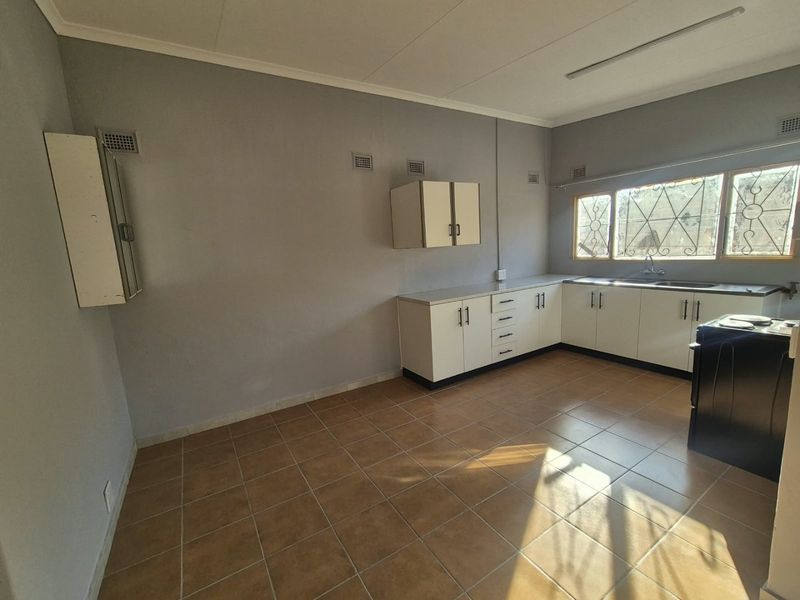 A functional, empty kitchen featuring tiled flooring, built-in cabinetry, and a stainless steel sink, ready for modernization or personal styling.