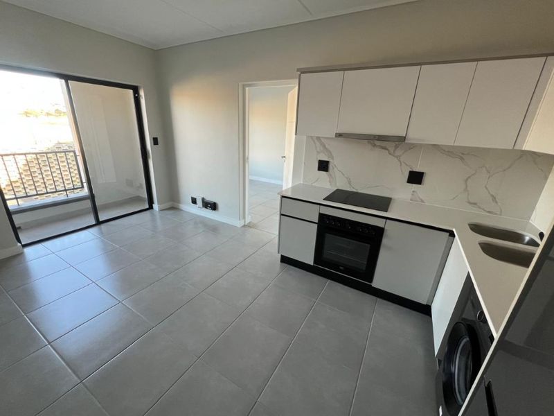 Modern open-plan kitchen and living area featuring sleek cabinetry, integrated appliances, tiled flooring, and direct access to a private balcony.