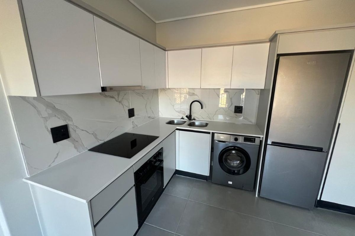 Modern kitchen featuring white cabinetry, marble-look splashback, integrated electric hob, oven, extractor fan, and a double sink with contemporary fixtures.
