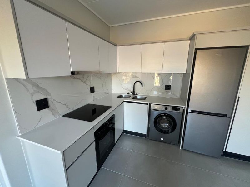Modern kitchen featuring white cabinetry, marble-look splashback, integrated electric hob, oven, extractor fan, and a double sink with contemporary fixtures.