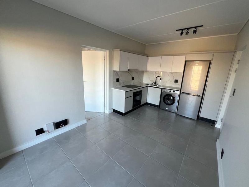 Modern open-plan kitchen featuring sleek white cabinetry, marble-look backsplash, integrated appliances, and neutral tiled flooring in a clean, contemporary apartment setting.