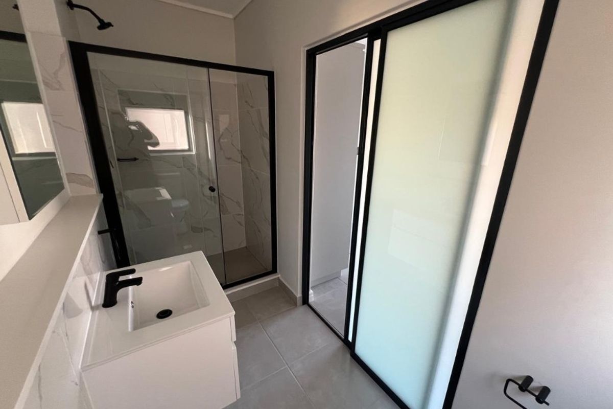 Modern bathroom featuring a walk-in shower with black-framed glass, a sleek vanity with a black mixer tap, and contemporary tiled finishes.