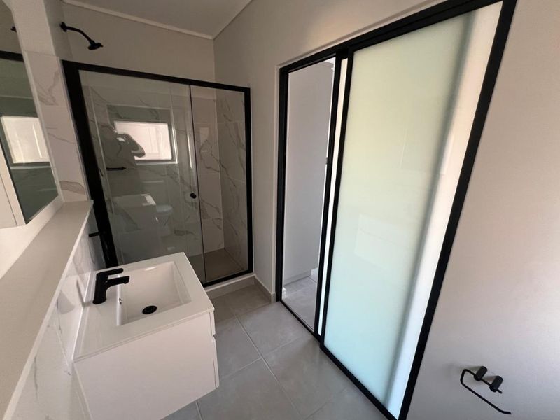 Modern bathroom featuring a walk-in shower with black-framed glass, a sleek vanity with a black mixer tap, and contemporary tiled finishes.