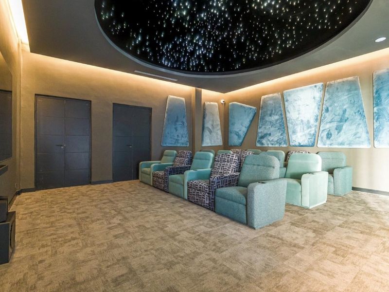 A dedicated cinema room featuring acoustic wall panels, carpeted flooring, and a decorative starlit ceiling design.