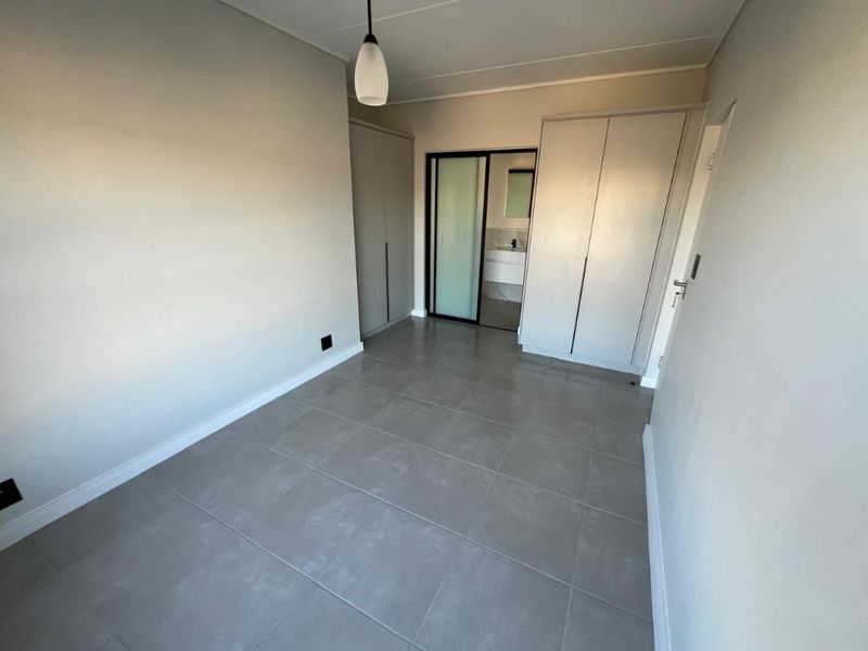 A clean, modern bedroom featuring neutral tiled flooring, ample built-in cupboard space, and direct access to an en-suite bathroom.