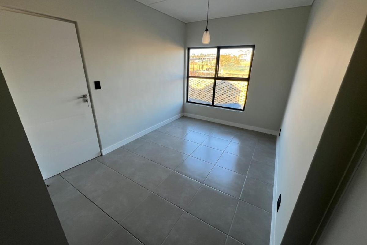 A bright, empty bedroom featuring neutral grey floor tiles, a modern pendant light, and a large window with black framing.