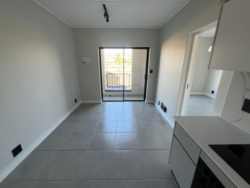 Modern open-plan living area featuring neutral tiled flooring, sleek kitchen cabinetry with stone countertops, and a sliding door leading to a private balcony.