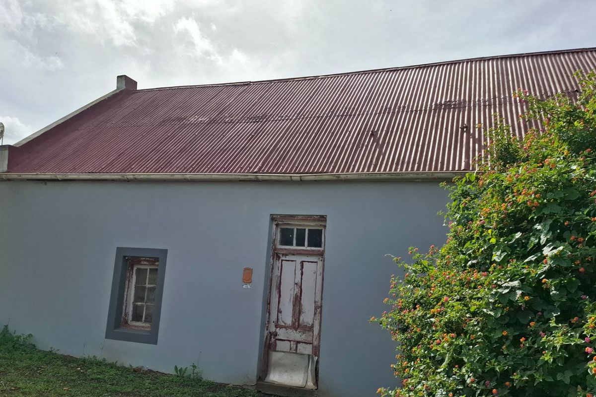 Rear elevation of a cottage featuring a corrugated metal roof, painted masonry walls, and a weathered timber entrance door.