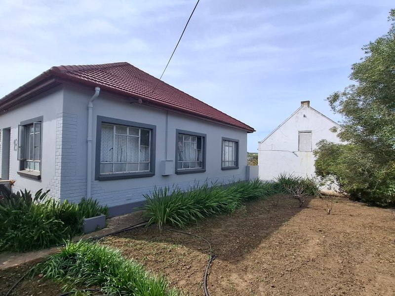 Rear view of a single-story house featuring a tiled roof, painted brick exterior, and established garden beds along the building perimeter.