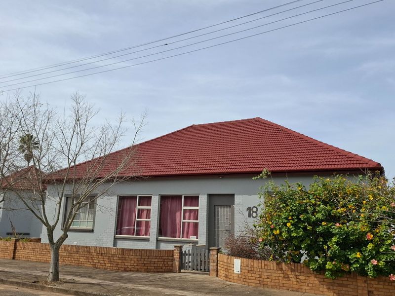 Front view of a single-story house featuring a red tiled roof, grey painted brick exterior, and a low brick boundary wall.