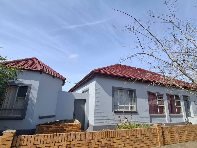 Front elevation of a single-story house featuring a painted brick facade, tiled roof, and a low brick boundary wall.