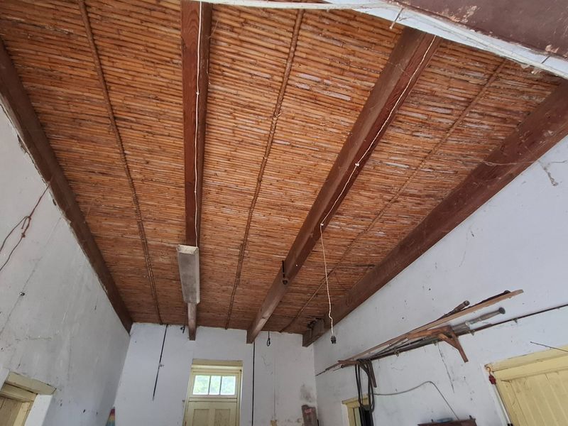 A utility space featuring an exposed timber beam and bamboo ceiling, requiring cosmetic renovation and wall repairs.