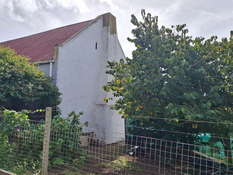 A view of the rear exterior elevation featuring a gabled roof structure and wire fencing, showing signs of weathering and exterior wear.