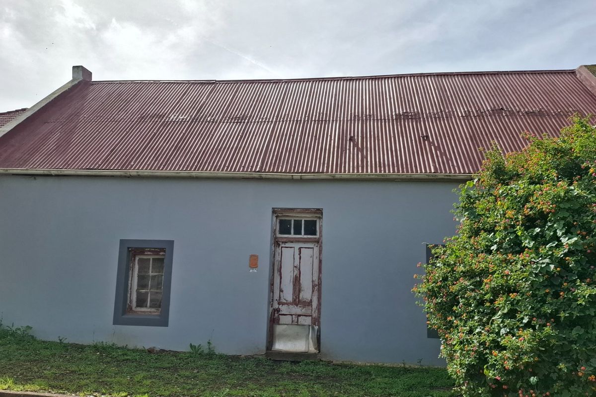 Front elevation of a cottage featuring a corrugated metal roof, painted exterior walls, and a weathered timber entrance door.