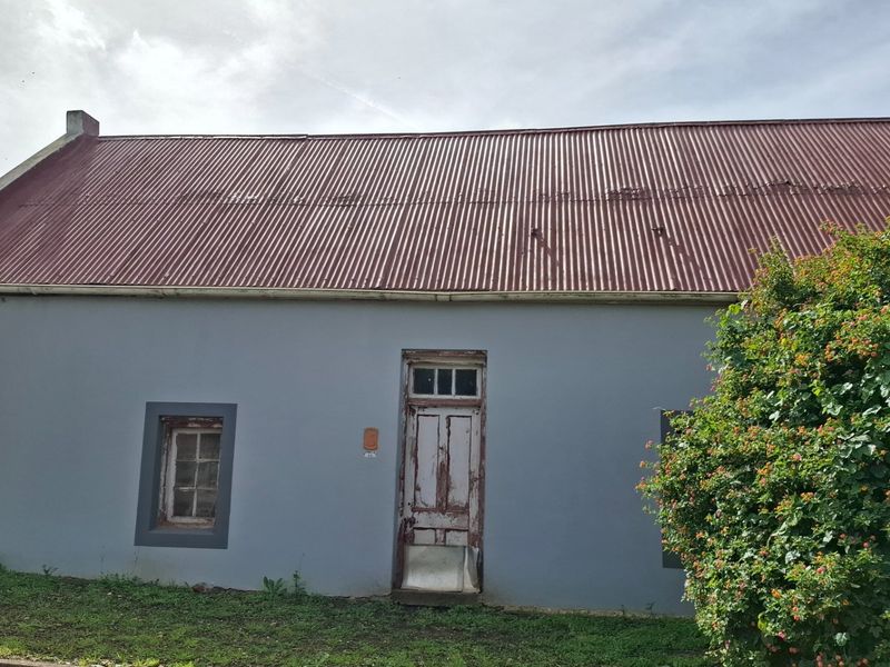 Front elevation of a cottage featuring a corrugated metal roof, painted exterior walls, and a weathered timber entrance door.