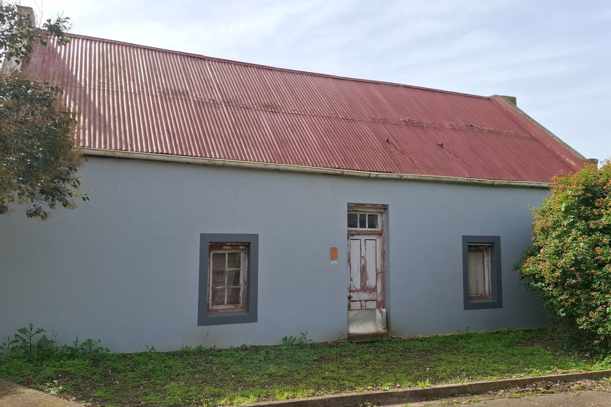 Front elevation of a cottage featuring a corrugated metal roof, timber-framed windows, and a weathered entrance door.