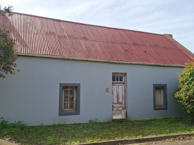 Front elevation of a cottage featuring a corrugated metal roof, timber-framed windows, and a weathered entrance door.