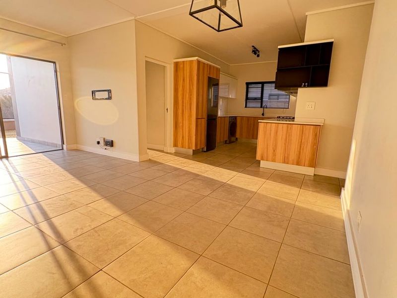 Spacious open-plan living and kitchen area featuring modern wood-finish cabinetry, tiled flooring, and direct access to an outdoor patio through a sliding glass door.