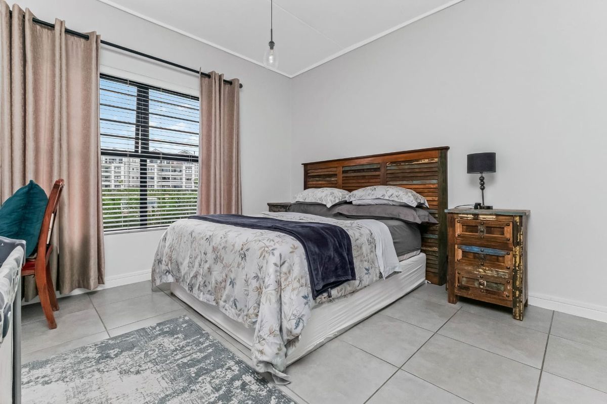 A well-maintained bedroom featuring neutral tiled flooring, a large window with blinds, and a simple pendant light fixture.