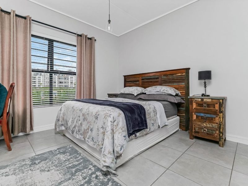A well-maintained bedroom featuring neutral tiled flooring, a large window with blinds, and a simple pendant light fixture.