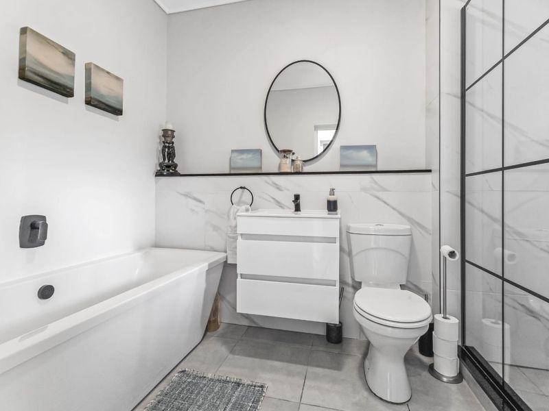 Modern bathroom featuring a freestanding bathtub, wall-mounted vanity, toilet, and a walk-in shower with a stylish black frame and marble-look wall tiles.