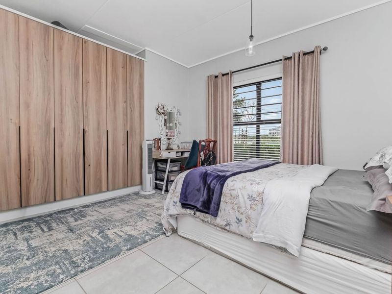 A well-maintained bedroom featuring large built-in wooden wardrobes, neutral tiled flooring, and a window with security bars for added safety.