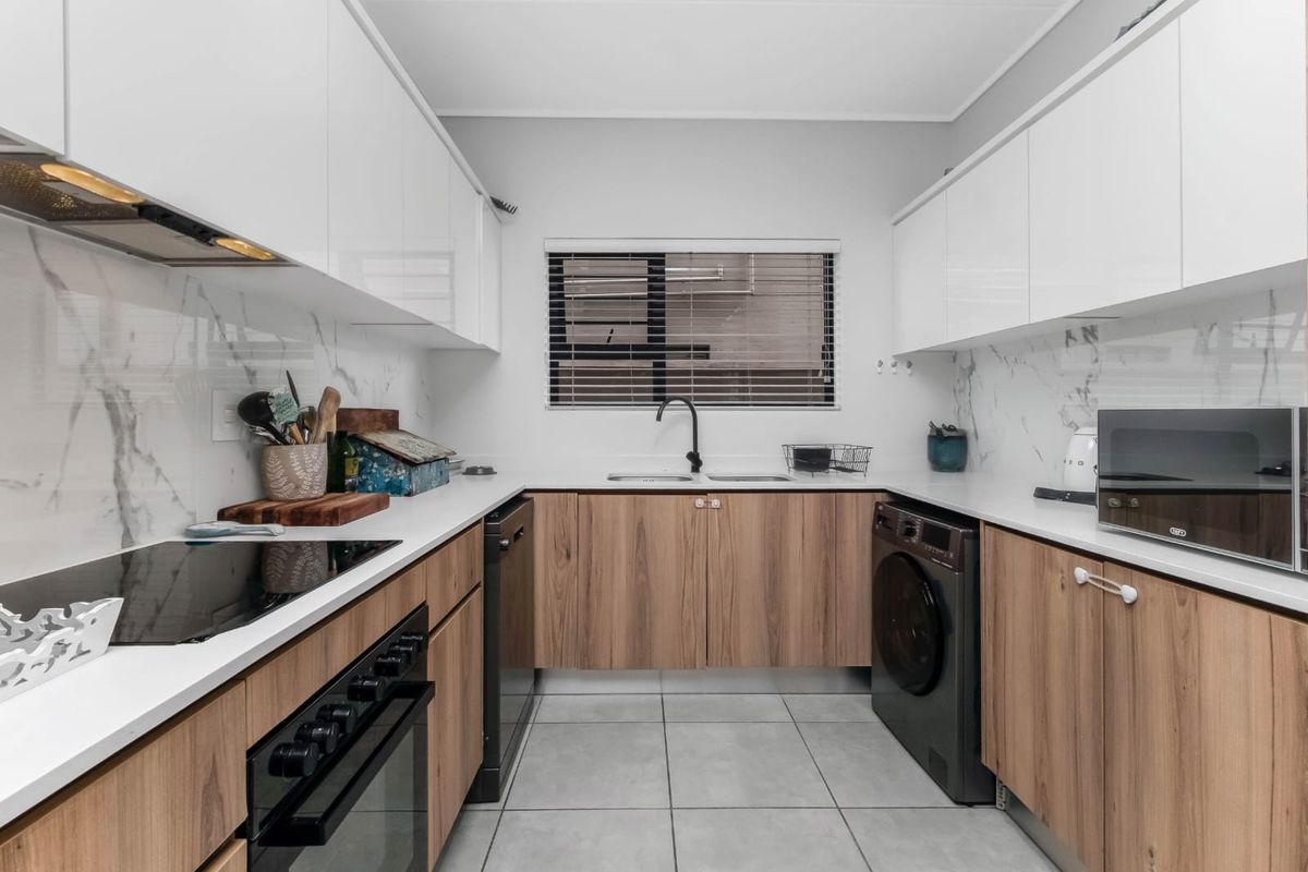 Modern galley-style kitchen featuring sleek wood-grain cabinetry, white stone countertops, marble-look splashbacks, and integrated appliances with high-quality finishes.