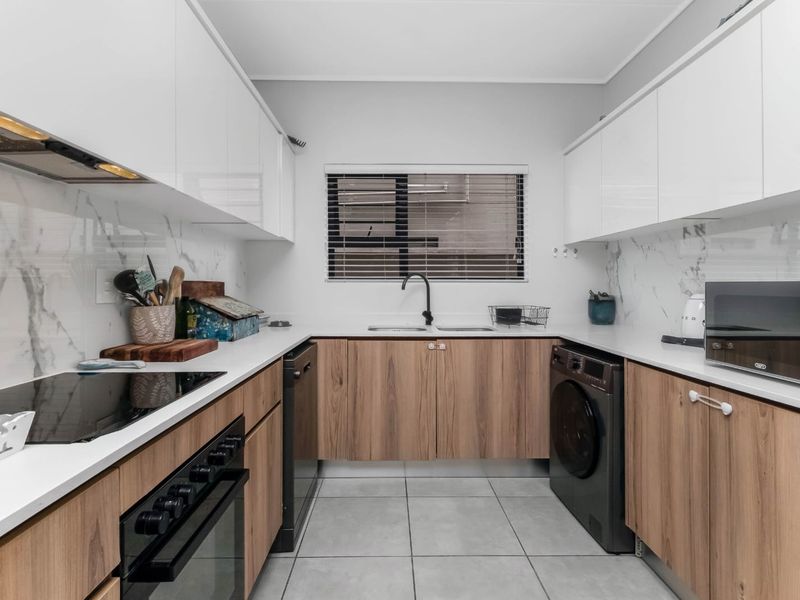 Modern galley-style kitchen featuring sleek wood-grain cabinetry, white stone countertops, marble-look splashbacks, and integrated appliances with high-quality finishes.