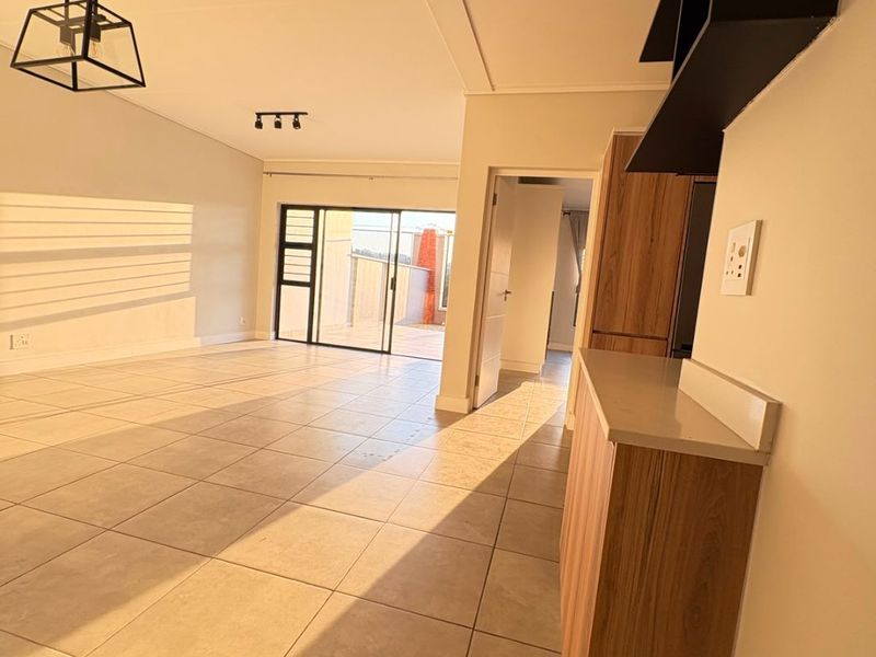 Spacious open-plan living area featuring tiled floors, modern cabinetry, and a sliding door leading to an outdoor balcony.