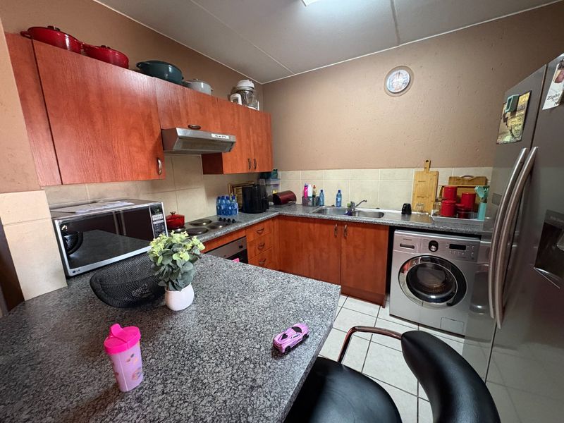 A functional kitchen featuring laminate cabinetry, granite countertops, a tiled backsplash, and integrated appliances including an oven, hob, and washing machine.