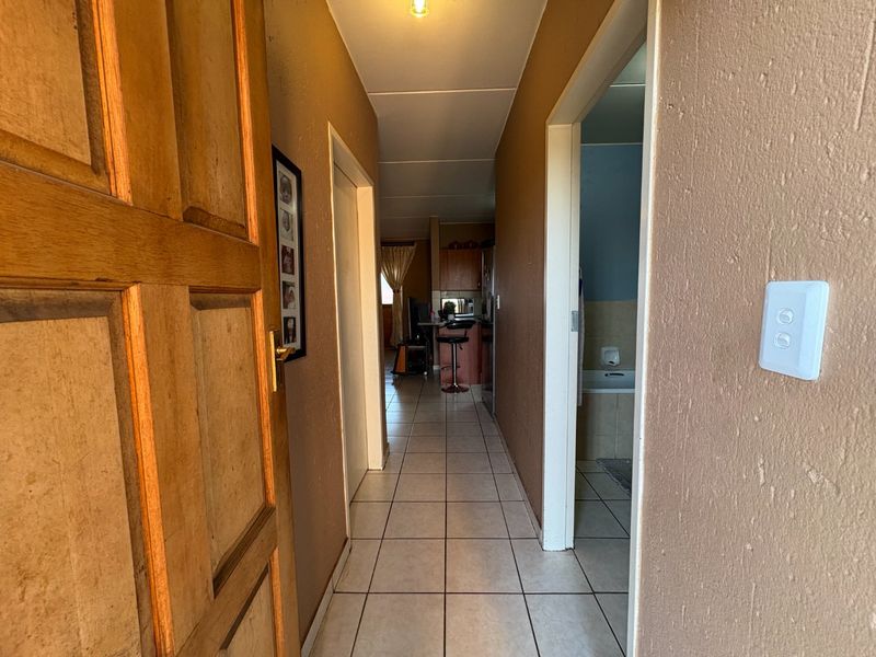 A narrow hallway with tiled flooring providing access to the kitchen and bathroom areas, featuring a solid timber entrance door.