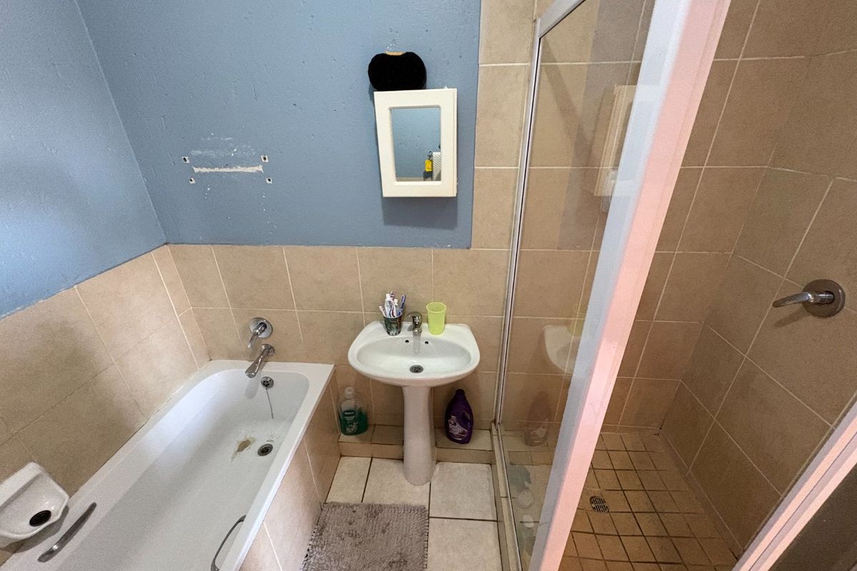 Bathroom featuring a bathtub, pedestal basin, and separate shower enclosure with tiled finishes. Requires cosmetic updates and repairs to wall surfaces.