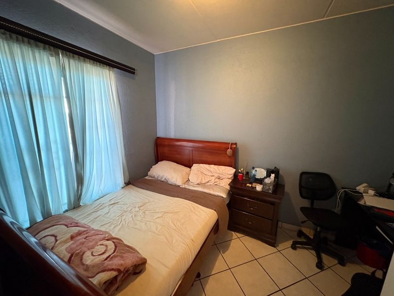 A functional bedroom featuring tiled flooring and a window with a curtain rail, providing a simple and practical living space.