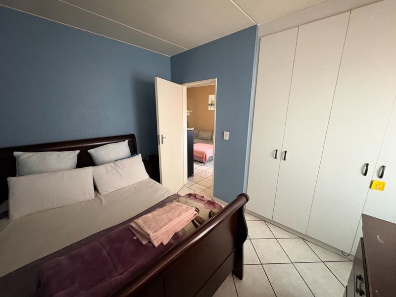 A bedroom featuring built-in cupboards and tiled flooring, with a view into an adjacent room.