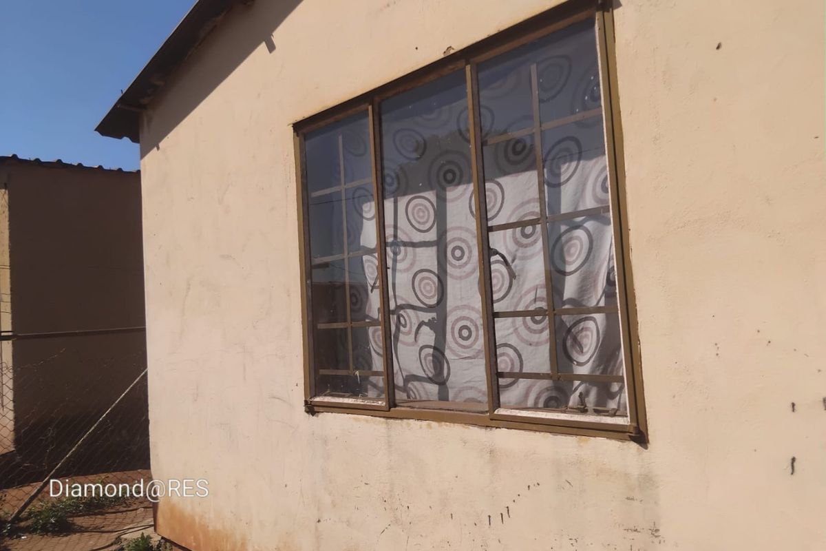 Exterior view of a residential building featuring a window with security burglar bars and plastered wall finishes showing signs of wear.